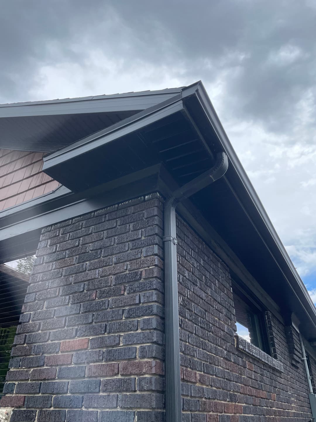 Close-up of a modern brick home showcasing eaves, guttering, and overcast sky.