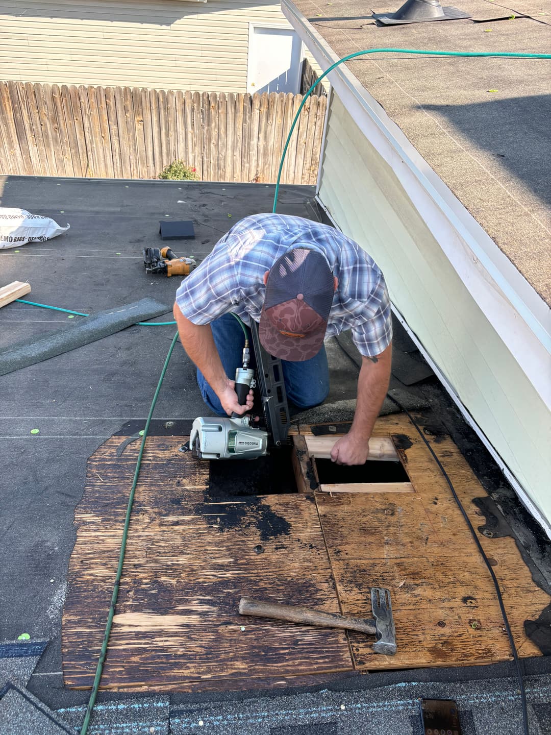 Person repairing a roof by replacing damaged plywood with tools on a sunny day.