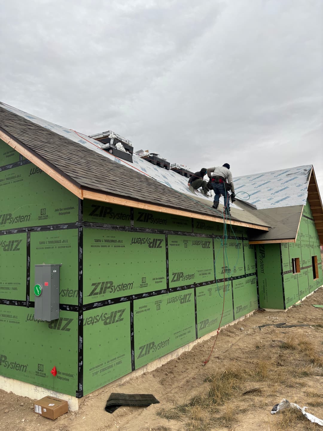 Workers installing roofing on a house under construction with ZIP System sheathing.