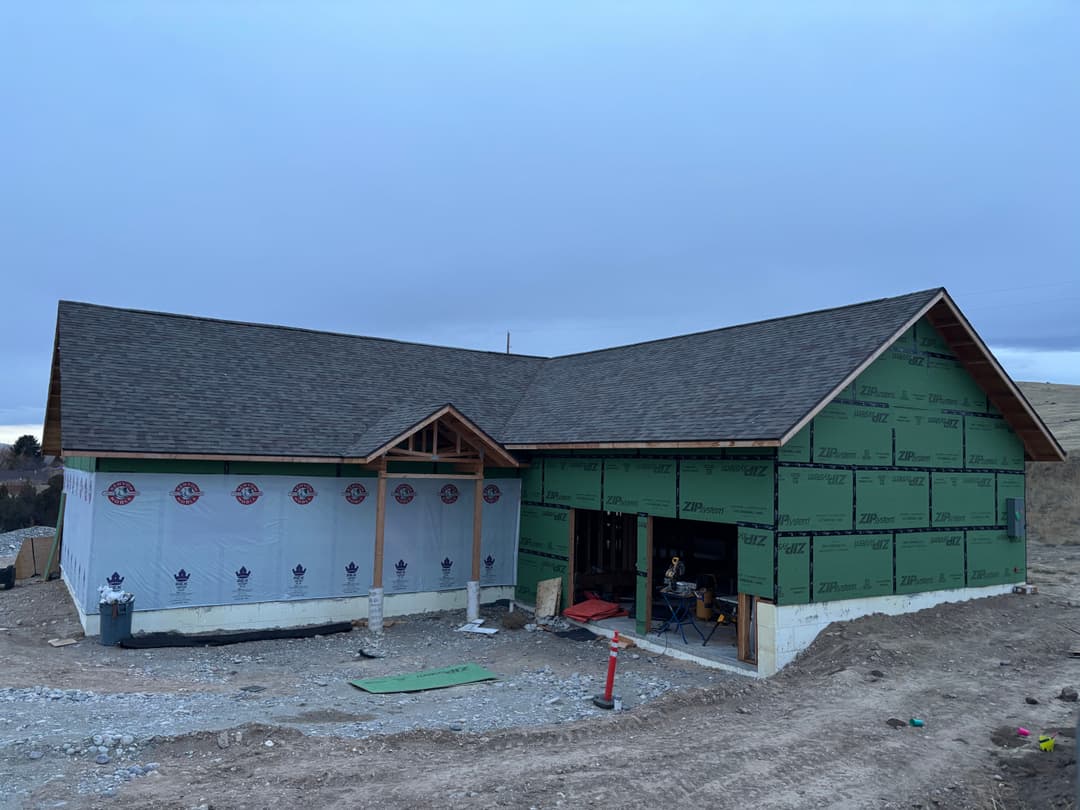 Newly constructed house with green sheathing and a shingled roof in a rural setting.