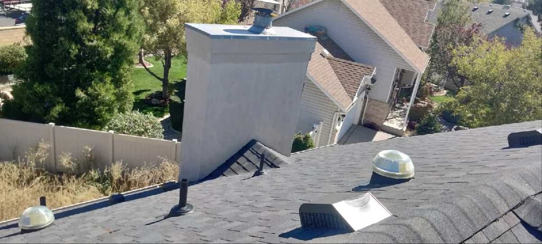 Aerial view of a residential roof with skylights and a chimney in a suburban area.