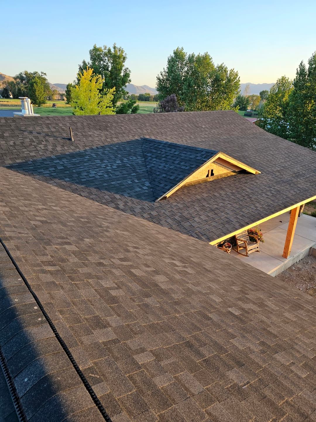 Aerial view of a gray shingle roof on a house surrounded by trees and mountains.